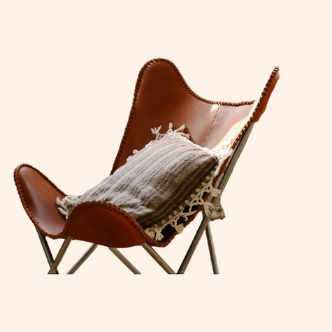 Stylish brown leather butterfly chair with a decorative pillow.